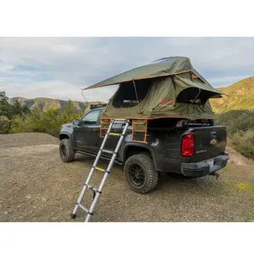 Black truck with a green rooftop tent and ladder in a mountainous landscape.
